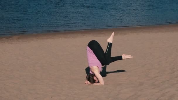Mujer haciendo yoga en la playa junto al río en la ciudad. Hermosa vista. Soporte de mano. Torzal en el aire . — Vídeo de stock