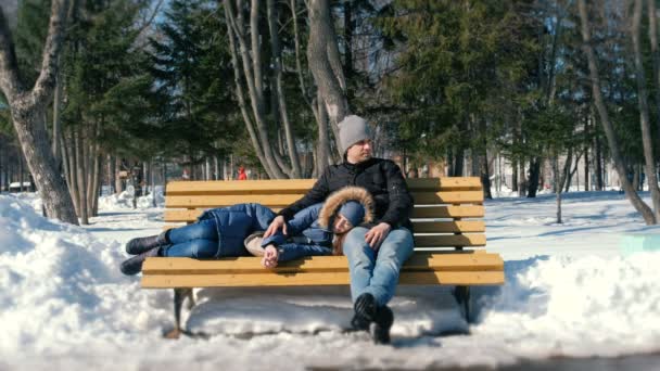Мужчина и женщина отдыхают вместе на скамейке в зимнем городском парке. Солнечный зимний день . — стоковое видео