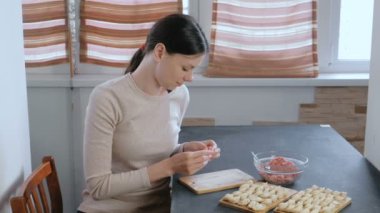 Kadın kıyma etli köfte yapar, kamera ve gülümsüyor görünüyor.