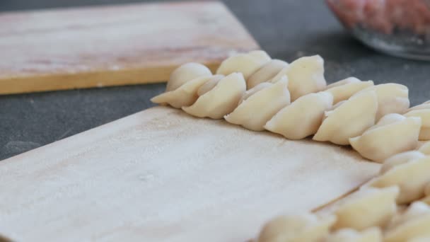 Vrouw maakt dumplings met gehakt vlees, close-up handen. Dumplings zet op houten plank. — Stockvideo