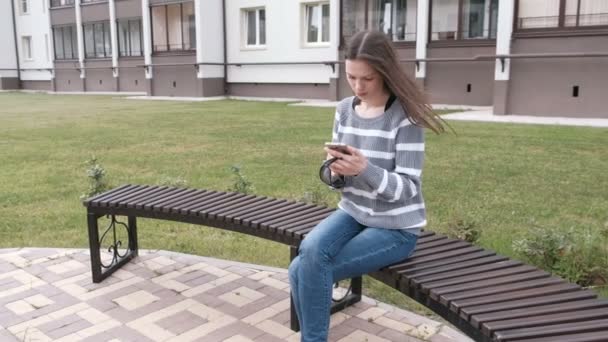 Vrouw eist mobiele telefoon zittend op het bankje in de buurt van het huis. — Stockvideo