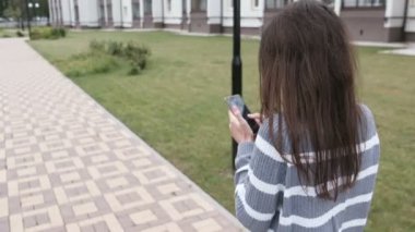 Tanınmayan esmer kadın eve yakın yürüyüş cep telefonunda bir mesaj türleri. Arkadan görünüm.