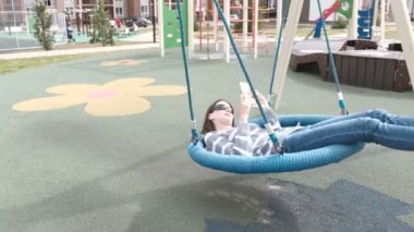 Kadın boş perdeli salıncakta sallanan ve tipik bir haber üstünde hareket eden telefon.