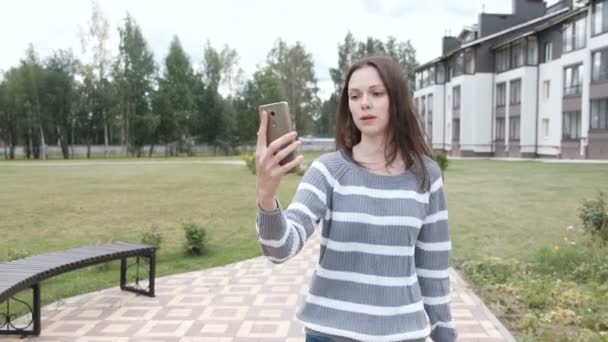 Mooie brunette vrouw blogger praten een video-chat op mobiele telefoon wandelen in de buurt van het huis. — Stockvideo