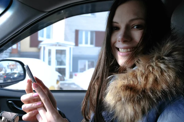 Uma mulher num carro com um telemóvel. Jovem bela mulher morena olhando para a câmera . — Fotografia de Stock