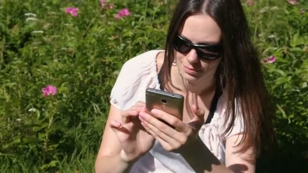 Frau tippt an sonnigem Tag im Park eine Nachricht aufs Handy. — Stockvideo