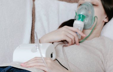 Nebulizatör ve astım tedavisi için kullanın. Genç kadın kanepede yatan inhaler maskesi aracılığıyla teneffüs edilmesi. Yan görünüm.