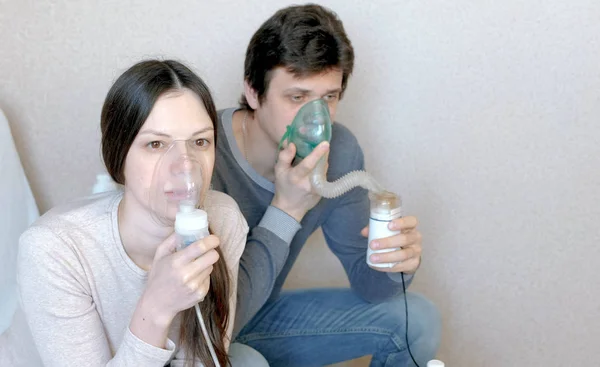 W leczeniu za pomocą rozpylacza i inhalator. Mężczyzna i kobieta wdechu przez inhalator maski. Widok z przodu zbliżenie. — Zdjęcie stockowe