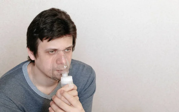 Vernevelaar en inhalator gebruiken voor de behandeling. Jongeman inademen door inhalator masker. Vooraanzicht — Stockfoto