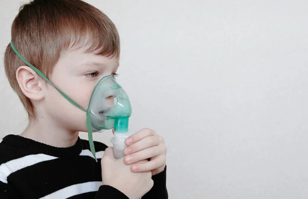 W leczeniu za pomocą rozpylacza i inhalator. Chłopiec wdechu przez inhalator maski. Widok z boku. — Zdjęcie stockowe