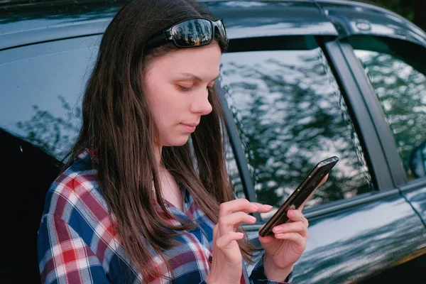 Женщина отправляет сообщение по телефону, стоящему рядом с машиной . — стоковое фото
