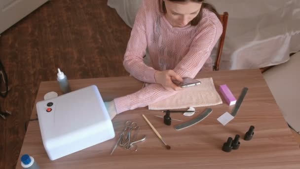 Vrouw droogt haar nagels met schellak in UV-lamp en surfen op internet in de mobiele telefoon. Bovenaanzicht. — Stockvideo