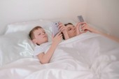 Máma a syn Probuď se a prohlížení internetu v jejich mobilních telefonů. Boční pohled.