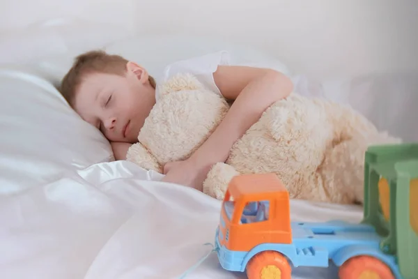 Menino de sete anos dormindo com seus brinquedos urso e carro de plástico . — Fotografia de Stock