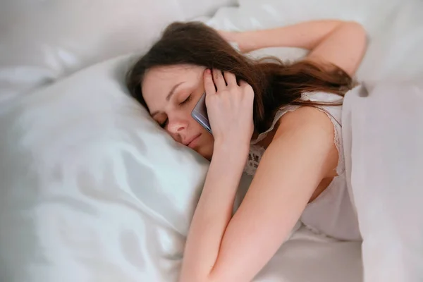 Young brunette woman wakes up from ring of a mobile phone, and speaks phone.