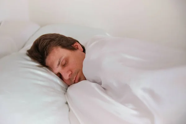 Ο άνθρωπος κοιμάται στο κρεβάτι μόνο κάτω από την κουβέρτα. Πλάγια όψη. — Φωτογραφία Αρχείου