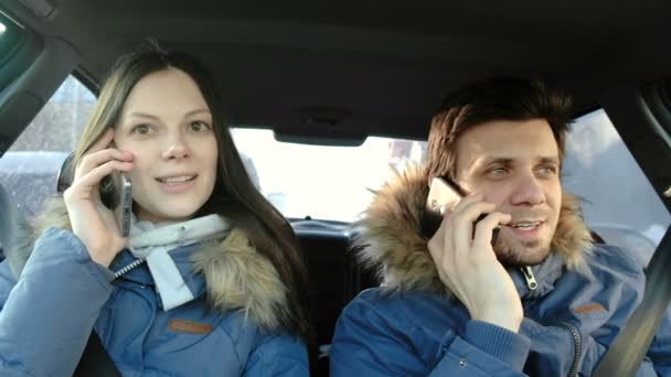 Man en vrouw spreken hun cellphones en lachend in auto zit. Vooraanzicht. — Stockvideo