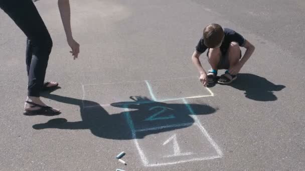 Mère et fils dessinent ensemble de la marelle sur le trottoir . — Video