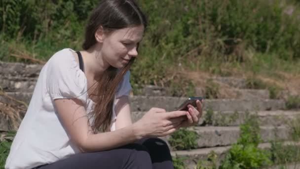 Fiatal nő ül a parkban mobiltelefon beszél. — Stock videók