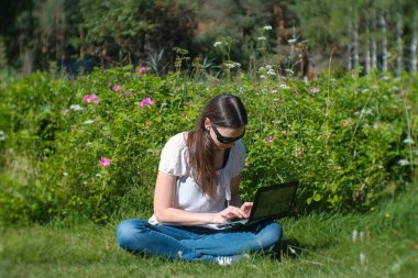 Yaz aylarında parkta oturan dizüstü bilgisayarda yazarak çalışma güzel esmer kız.