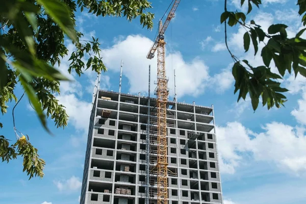 Многоэтажное строящееся жилое здание со строительным краном на фоне дерева и неба . — стоковое фото