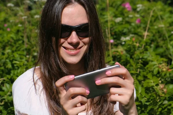 Mujer está jugando un juego en el teléfono móvil sentado en el parque en el día soleado . — Foto de Stock