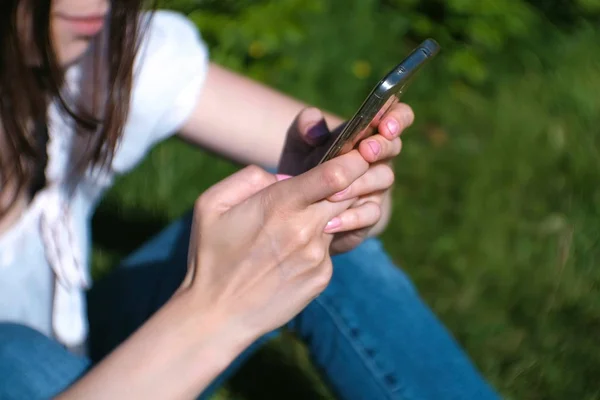 La mujer está escribiendo un mensaje en el teléfono móvil sentado en el parque en el día soleado, charlando. Primer plano de las manos . — Foto de Stock