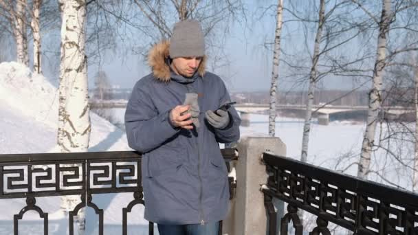 Hombre de chaqueta azul con capucha de piel limpia la pantalla del teléfono con guantes en invierno Park . — Vídeos de Stock