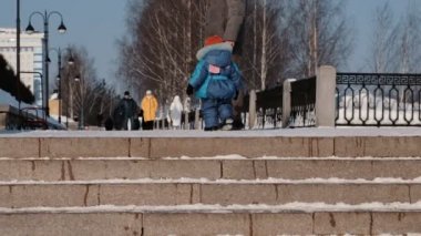 Tanınmaz halde çocuk babası yanında karlı merdiven ile kış parkta yürüyor.