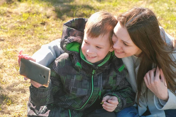 Mamá e hijo hacen selfie en el teléfono móvil en el parque de primavera . — Foto de Stock