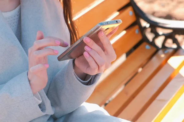 Frau tippt eine Nachricht in ihr Telefon sitzt auf der Bank im Park. Hände aus nächster Nähe. — Stockfoto