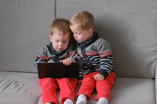 Two twin brothers take away each others tablet sitting on the sofa. Kids play games on the tablet. — Stock Photo, Image