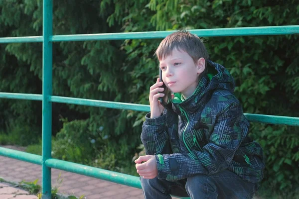 Chłopiec wzywa telefonu i rozmowa siedzący w parku. — Zdjęcie stockowe