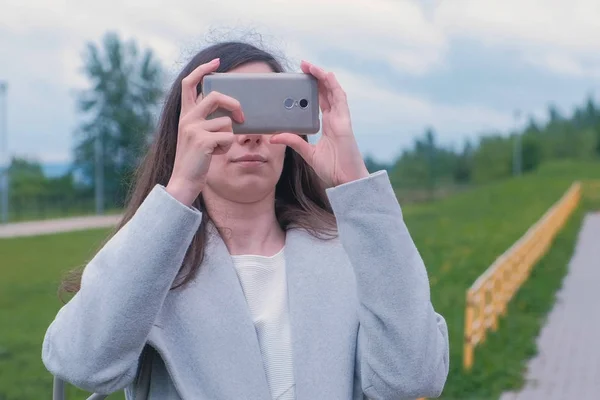 Young woman shoots a photo and video on a mobile phone on the Playground.