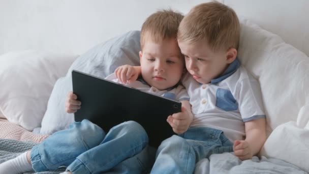 Niños con tableta. Dos niños gemelos niños pequeños mirando dibujos animados en la tableta acostado en la cama . — Vídeos de Stock