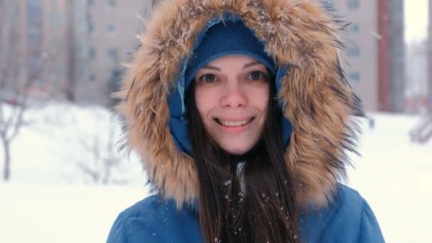 Young woman brunette looking at camera and smiling. Wearing blue down jacket with fur hood, face close-up. — Stock Video