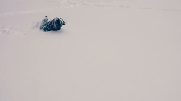 Niño tirado en la nieve rodando de lado a lado . — Vídeo de stock