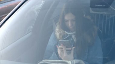 Genç esmer kadın mavi ceket seyir telefon aşağı arabanın ön cam ile göster.