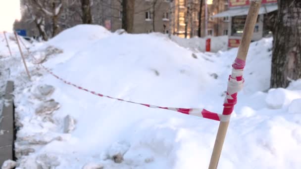 Κόκκινο και λευκό προσοχή ταινία στην άκρη του δρόμου στην πόλη. Ημέρα του χειμώνα και χιονοστιβάδες. — Αρχείο Βίντεο
