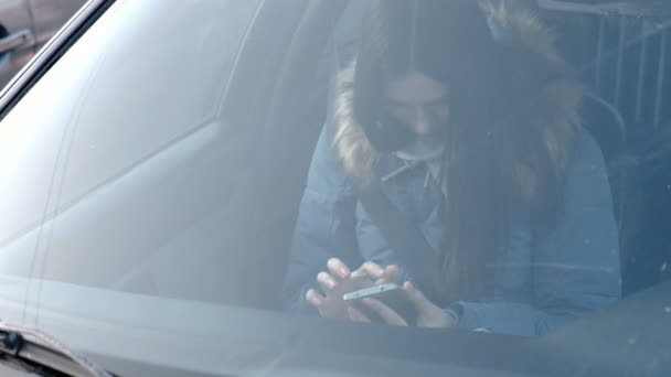 Blick durch die Windschutzscheibe des Autos auf eine Frau, die auf das Telefon schaut. Frontscheibe im Fokus. — Stockvideo