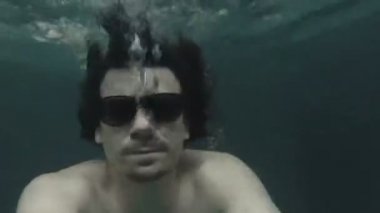 Erkek Güneş gözlüğü bir havuzda su altında yüzüyor.