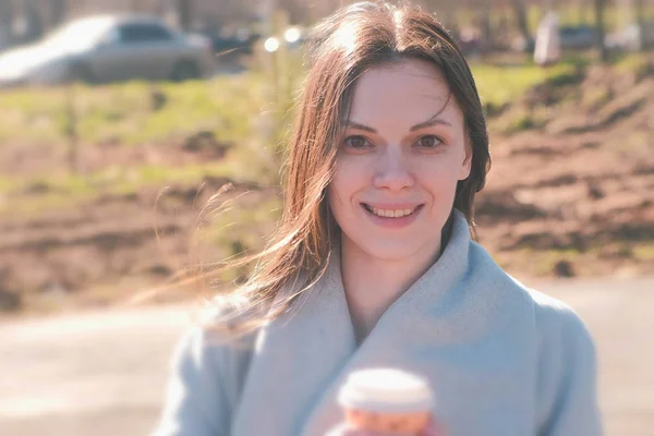 Retrato de jovem morena de casaco caminha no parque da cidade e bebe café. Primavera. . — Fotografia de Stock