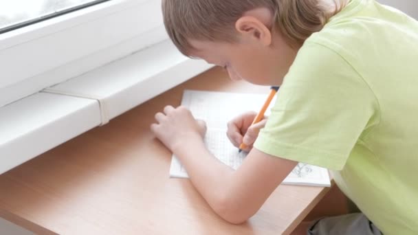 Menino da escola aprende a escrever cartas sentadas à mesa. Fazer trabalhos de casa . — Vídeo de Stock