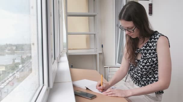 Kobieta pisze coś w sitiing notebook na balkonie w domu. Zobacz na drodze z okna. — Wideo stockowe