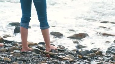 Kadın taş Beach'te dalgalar üzerinde duruyor. Kot yakın çekim Ayak.
