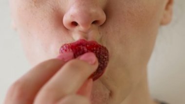 Kadın kırmızı dudaklar ile çilek yiyor. Ağız yakın çekim. Önden görünüm.
