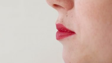 Kadın kırmızı dudaklar ile çilek yiyor. Ağız yakın çekim. Yan görünüm.