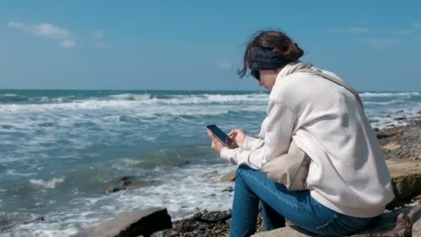 妇女玩游戏在电话坐在海岸边在秋季. — 图库视频影像