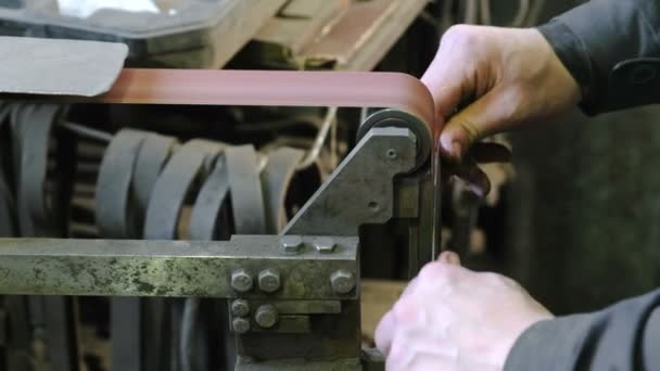 Slijpen billets van metalen mes op een riem-slijpmachine. Close-up van een mans hand. — Stockvideo