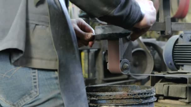 Slipning uppläggningar av metall kniv på ett bälte-slipmaskin. Närbild av en mans händer. — Stockvideo